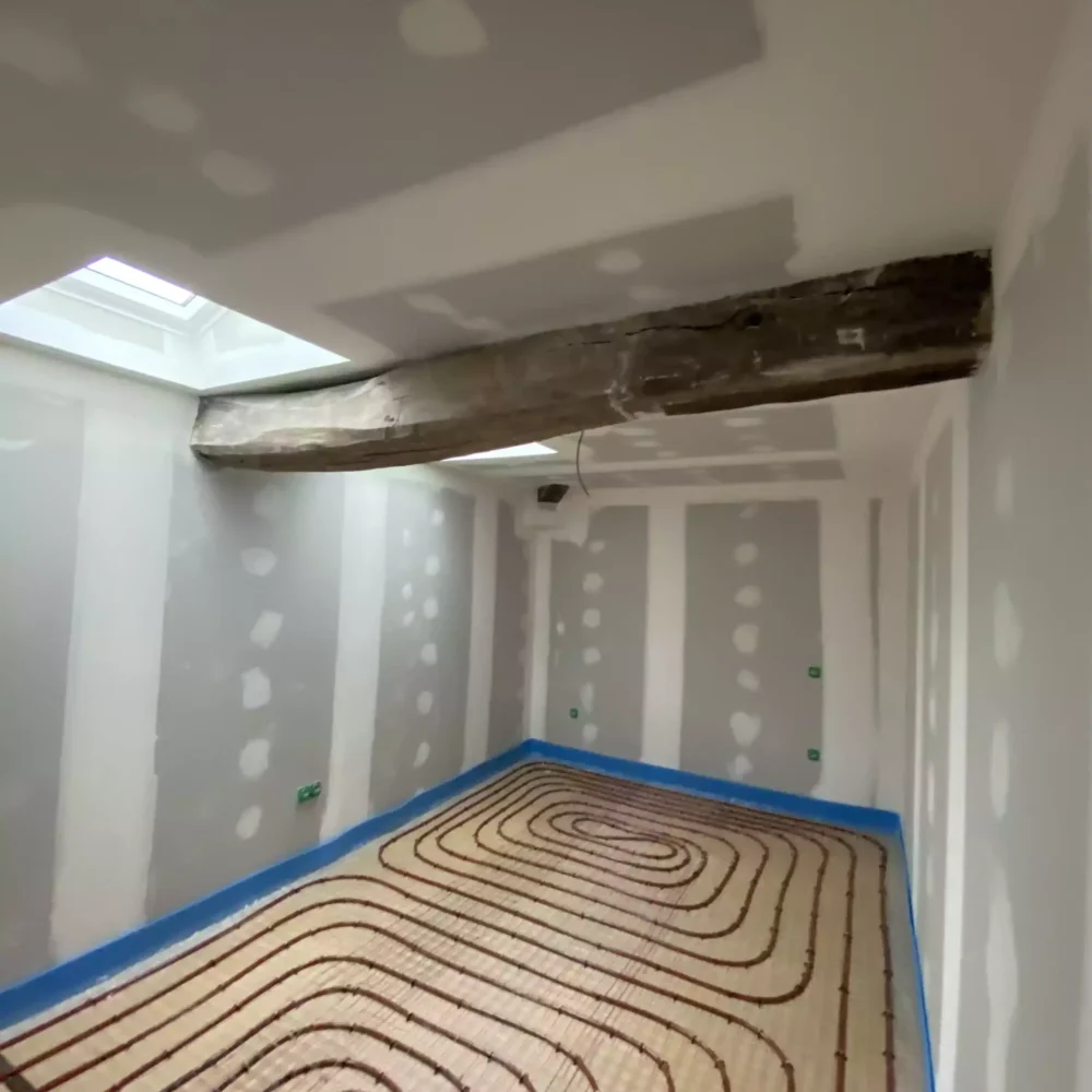 Installation des boucles de tubes pour plancher chauffant dans une zone de vie au rez-de-chaussée, intégrant la régulation domotique.