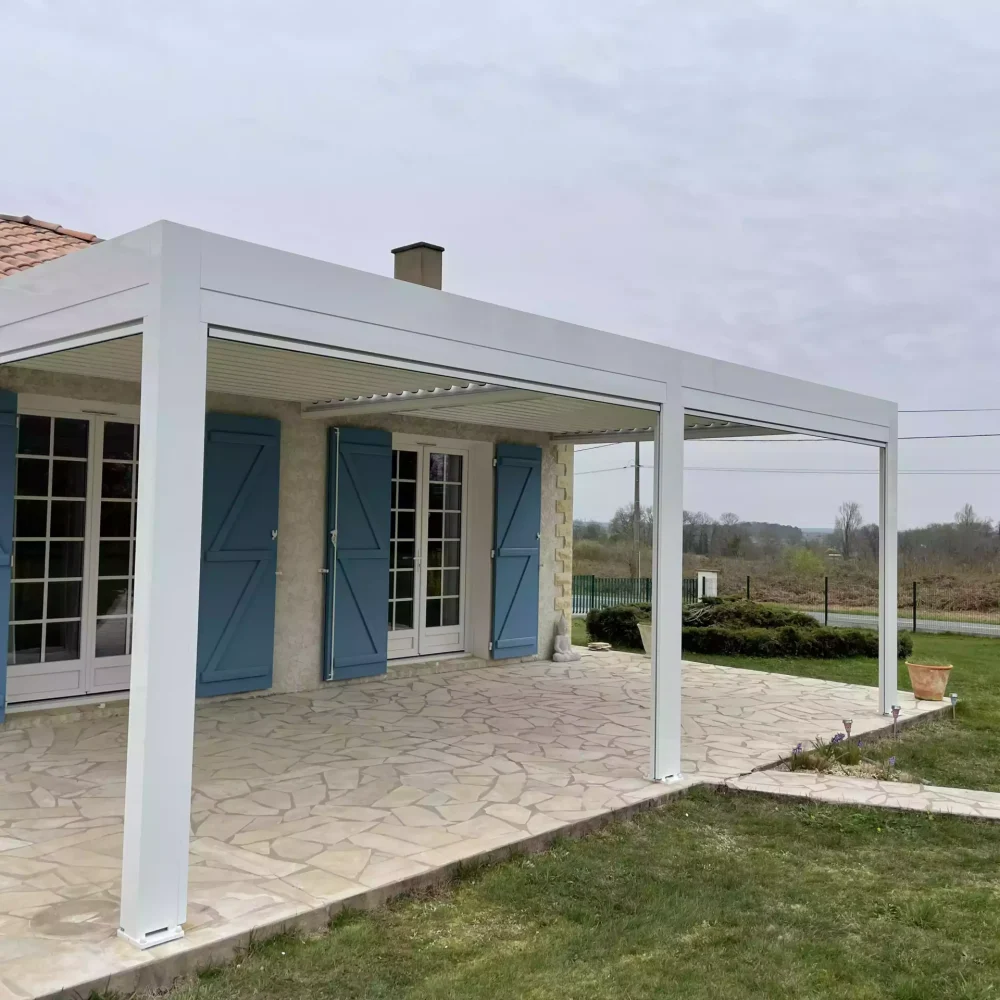 Pergola bioclimatique blanche installée devant une maison traditionnelle avec volets bleus, Nord Gironde.